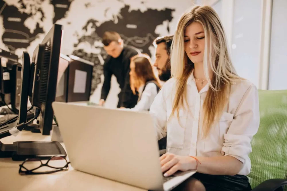 a confident woman working on her laptop with the team working in the background