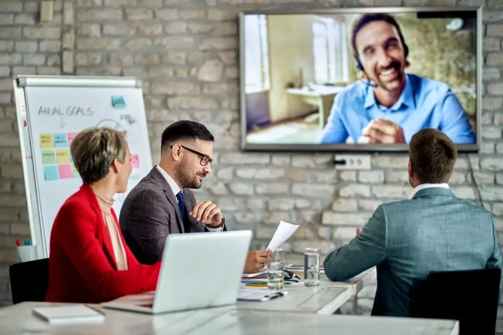 a team holding a remote meeting with part of the face-to-face team and part of the team on a screen on the wall