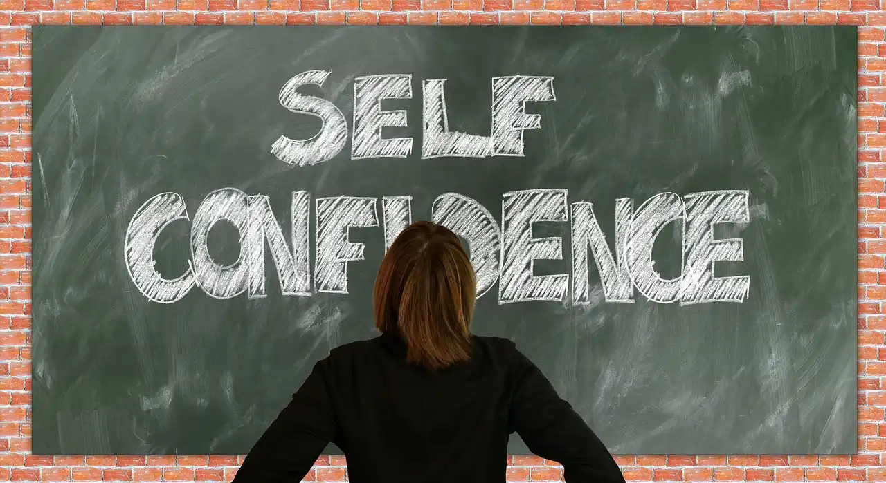 a woman in front of a blackboard with "self-confidence" written on it
