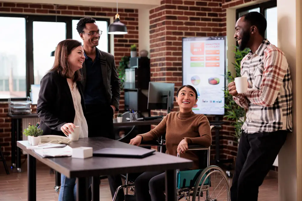a team in a meeting composed of diverse people, a black man, an Asian woman in a wheelchair, another woman and another man with glasses