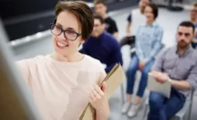 mentoring benefici: un mentore femminile che scrive su una lavagna con allievi seduti sullo sfondo