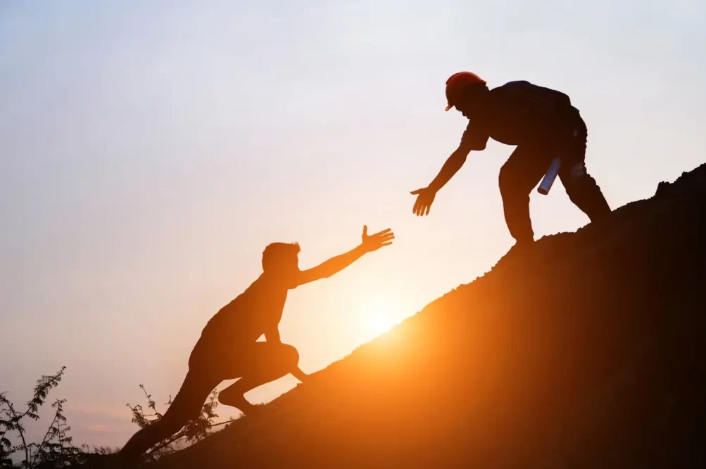mentoring power: a photo of two people on a mountain and the person higher up holding hands with the person lower down