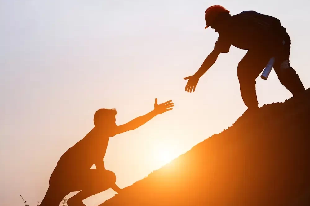 poder de la tutoria: una foto de dos personas en una montaña y la persona que está más arriba tomándose de la mano con la persona que está más abajo